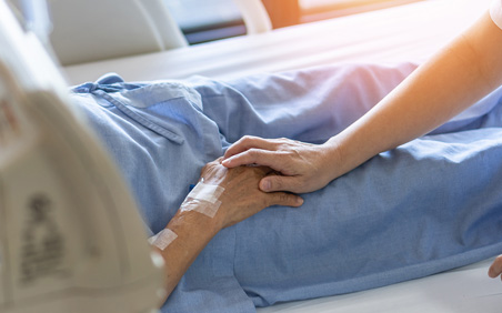 Nurse with holding palliative care patients hand in bed.